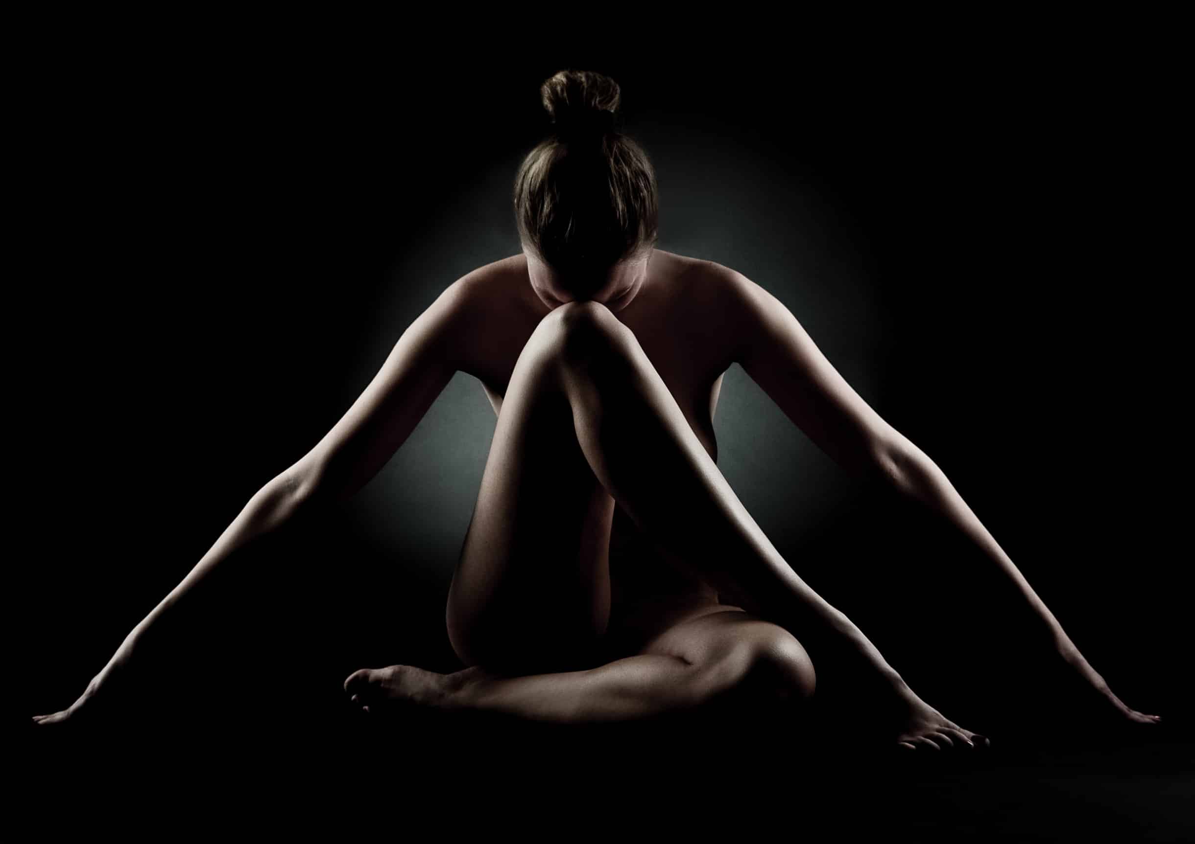 Künstlerische Fine Art Aktfotografie von René Lüdke in Hamburg – Frau sitzt mit ausgestreckten Armen, Kopf auf Knie.